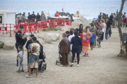 Varios migrantes recogen comida y bebida de Cruz Roja en la playa del Trampolín.