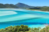 Vista panorámica de Whitehaven Beach en Australia, con aguas turquesa y arena blanca de sílice formando remolinos naturales entre colinas verdes.