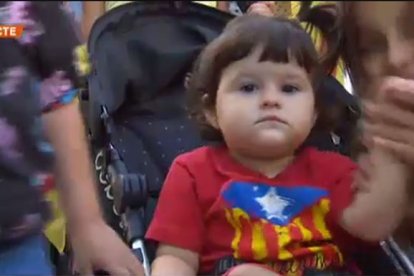 Una niña en su silla de paseo ataviada con una camiseta con la estelada impresa.