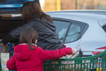 Una mujer y una niña meten la compra en el maletero del coche al salir de un supermercado.