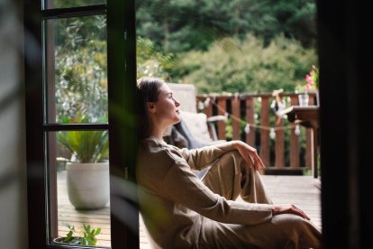 Mujer sentada junto a una ventana abierta, contemplando la naturaleza y disfrutando de un momento de serenidad personal.