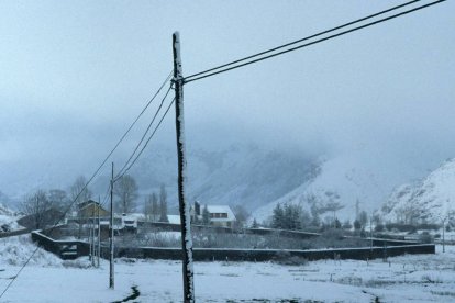 Pueblo de Babia cubierto de nieve con montañas al fondo y cables eléctricos en primer plano.