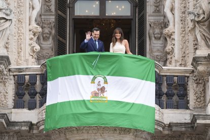 El presidente de la Junta de Andalucía, Juanma Moreno, despliega la bandera andaluza junto a la periodista Isabel Jiménez.