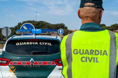 Agente de la Guardia Civil equipado con su chaleco reflectante, junto al coche patrulla en una carretera