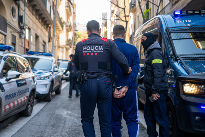 Un agente de los Mossos d'Esquadra se lleva a un detenido durante un operativo policial
