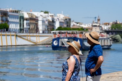 Personas con ropa veraniega paseando junto al río Guadalquivir en Sevilla.