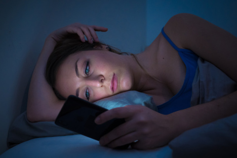 Una joven en la cama mira su móvil