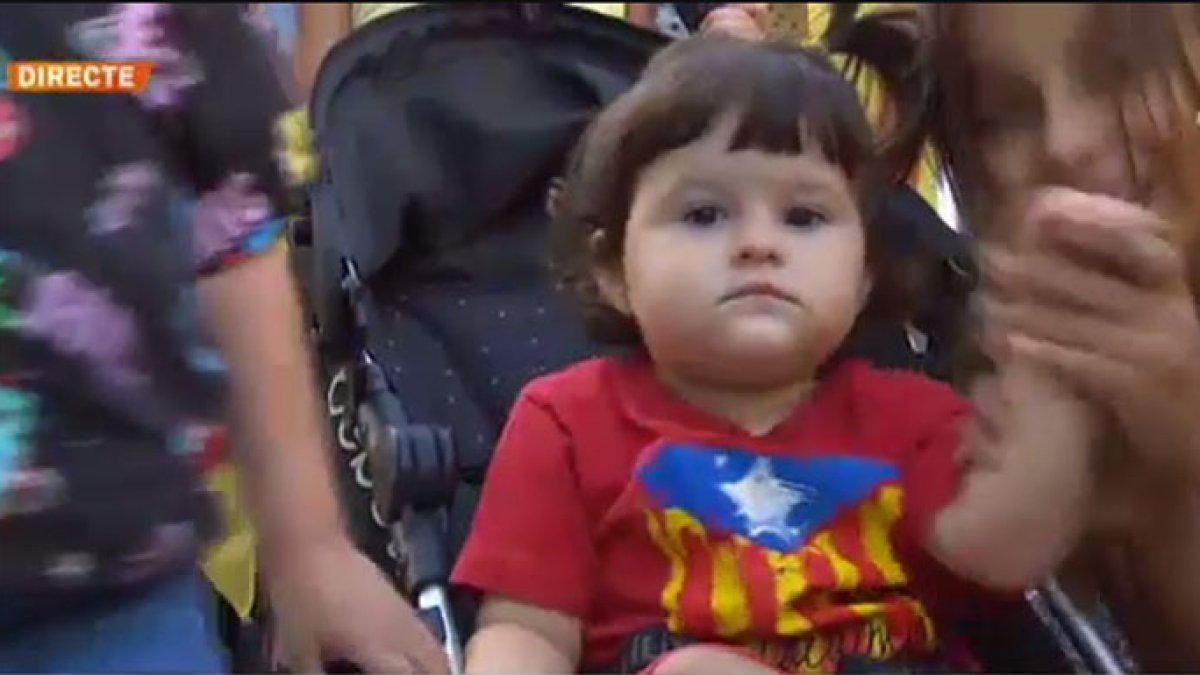 Una niña en su silla de paseo ataviada con una camiseta con la estelada impresa.