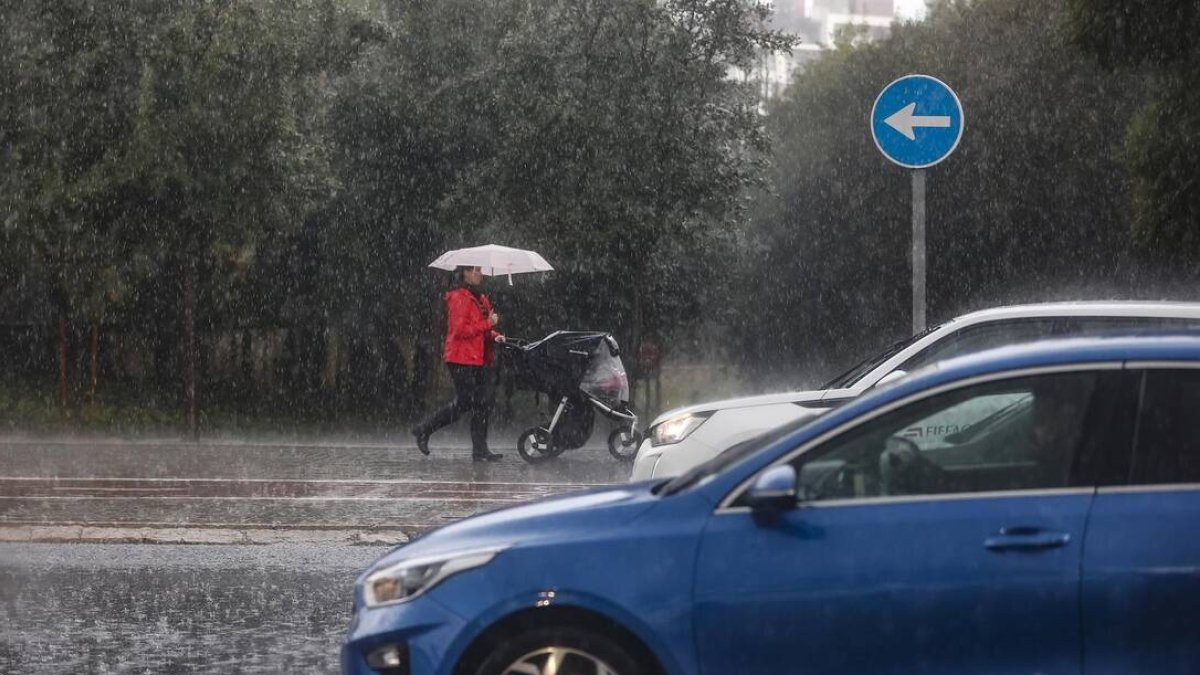 Una mujer lleva un carrito de bebé mientras se protege de la lluvia con un paraguas, - Rober Solsona - Europa Press