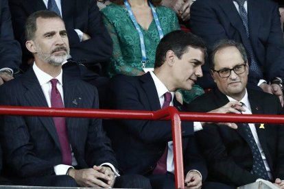 Felipe VI, en un gesto pensativo, mientras Sánchez y Torra conversan.