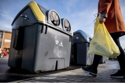 Una mujer depositando basura en un contenedor.