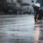 A couple with raincoat on a motorbike during hard rainfall/Dramatic scene of rainy season in Southeast Asia).Selective focus and very shallow depth of field composition