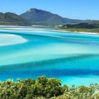 Vista panorámica de Whitehaven Beach en Australia, con aguas turquesa y arena blanca de sílice formando remolinos naturales entre colinas verdes.