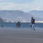 Varias personas caminan por la playa mientras les da el viento