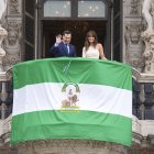 El presidente de la Junta de Andalucía, Juanma Moreno, despliega la bandera andaluza junto a la periodista Isabel Jiménez.