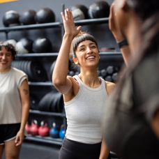 Compañeras celebran el final de su entrenamiento en el gimnasio, reflejando el auge de la actividad física como hábito de bienestar.