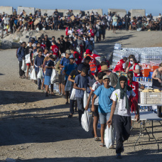 Miembros de la Cruz Roja reparten comida a los inmigrantes en la playa de El Trampolín en Ceuta.