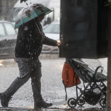 Un hombre lleva un carrito de bebé mientras se protege de la lluvia con un paraguas