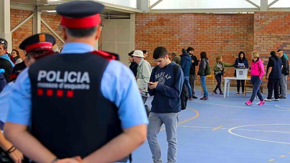 Un Mossos mira, de brazos cruzados, como gente va a votar en el referéndum ilegal.
