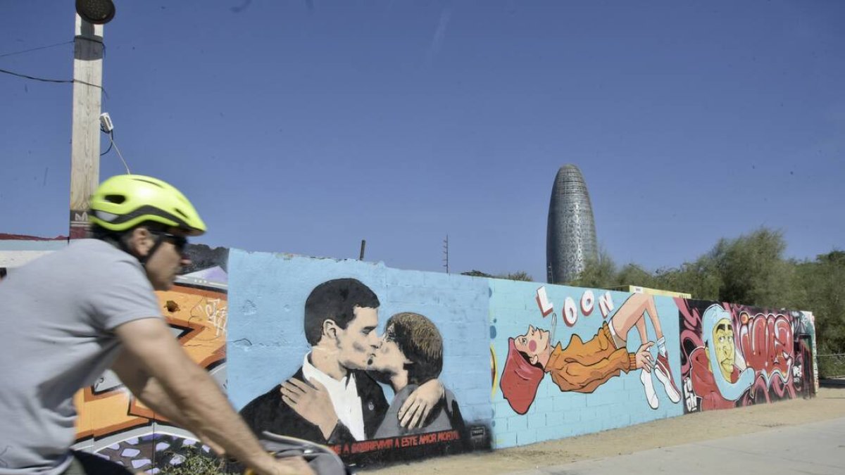 Un ciclista pasa al lado de la pintura del presidente Pedro Sánchez y al expresidente de la Generalitat y eurodiputado de Junts, Carles Puigdemont, dándose un beso en el mural del artista urbano TVBoy