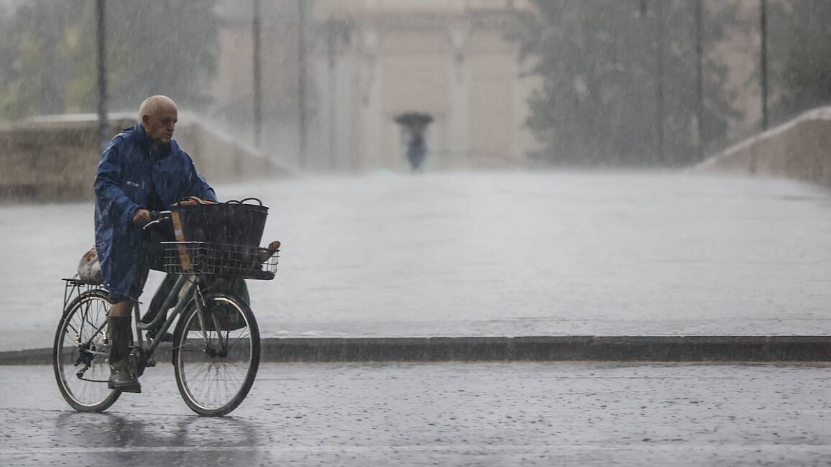 Imagen archivo persona bajo la lluvia de esta mañana en bicicleta por Valencia - EUROPA PRESS