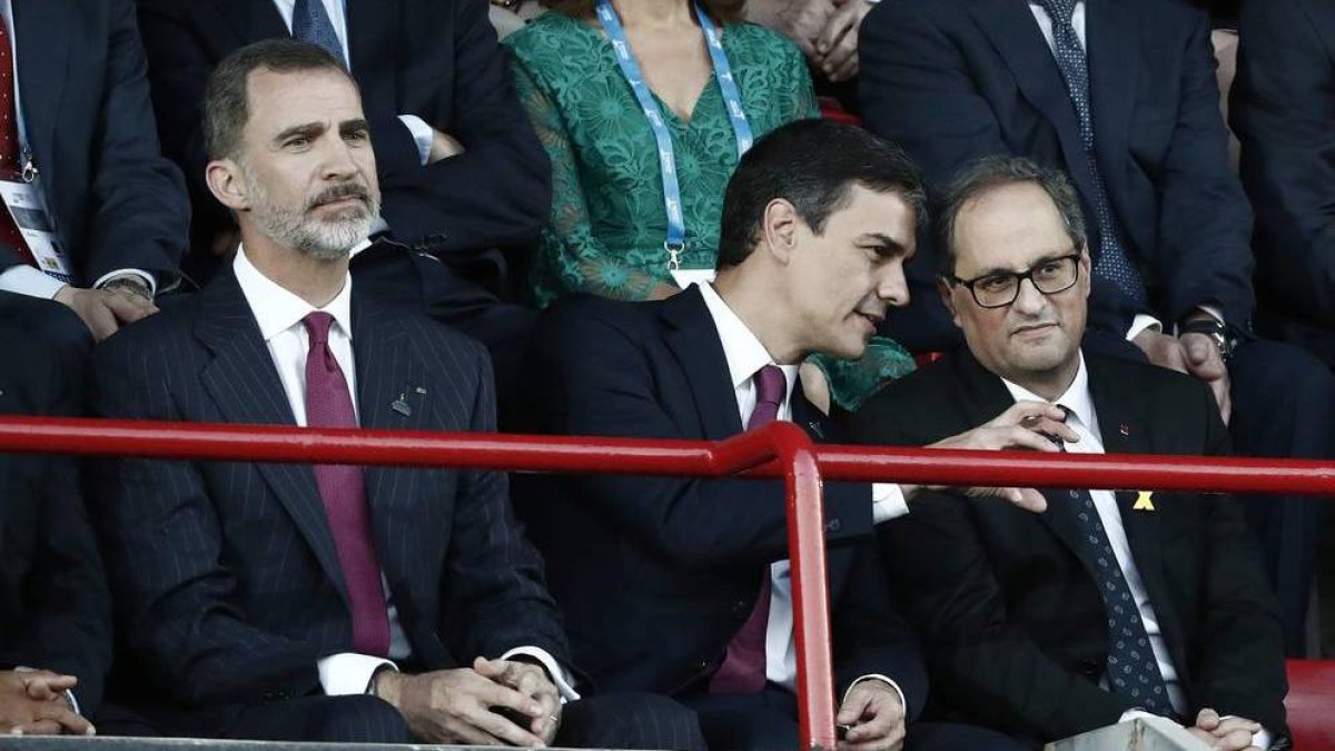 Felipe VI, en un gesto pensativo, mientras Sánchez y Torra conversan.