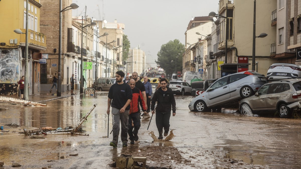 Varias personas recorren calles llenas de agua y barro tras el paso de la DANA por el barrio de La Torre de Valencia