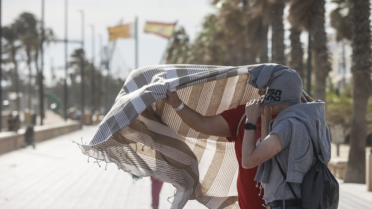 Dos personas se refugian del viento en el paseo de la playa de la Malvarrosa