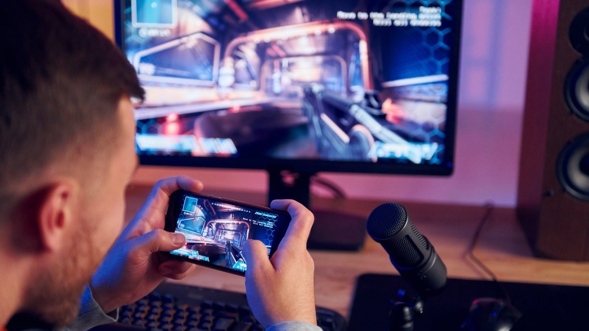 Using the smartphone. Online streamer playing FPS shooter game at home.