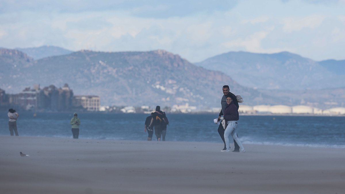 Varias personas caminan por la playa mientras les da el viento