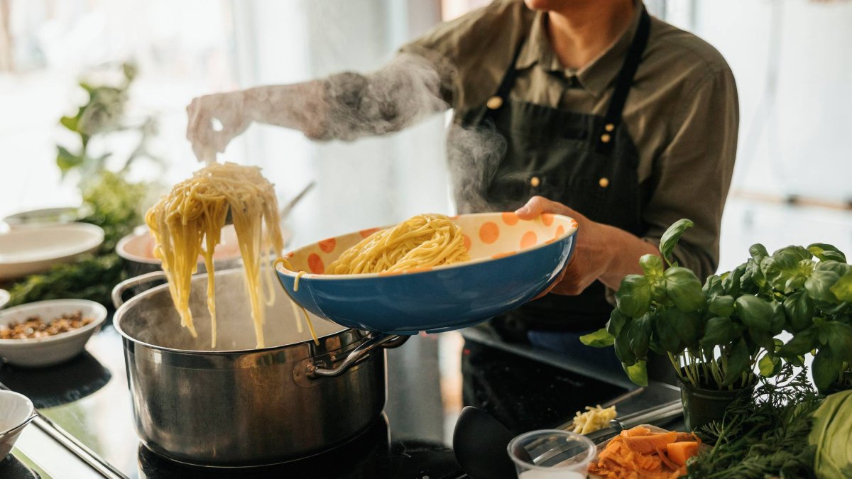 Preparación de pasta caliente en cocina doméstica con ingredientes frescos: una escena cotidiana que pone a prueba el uso de conservas como ingrediente principal.