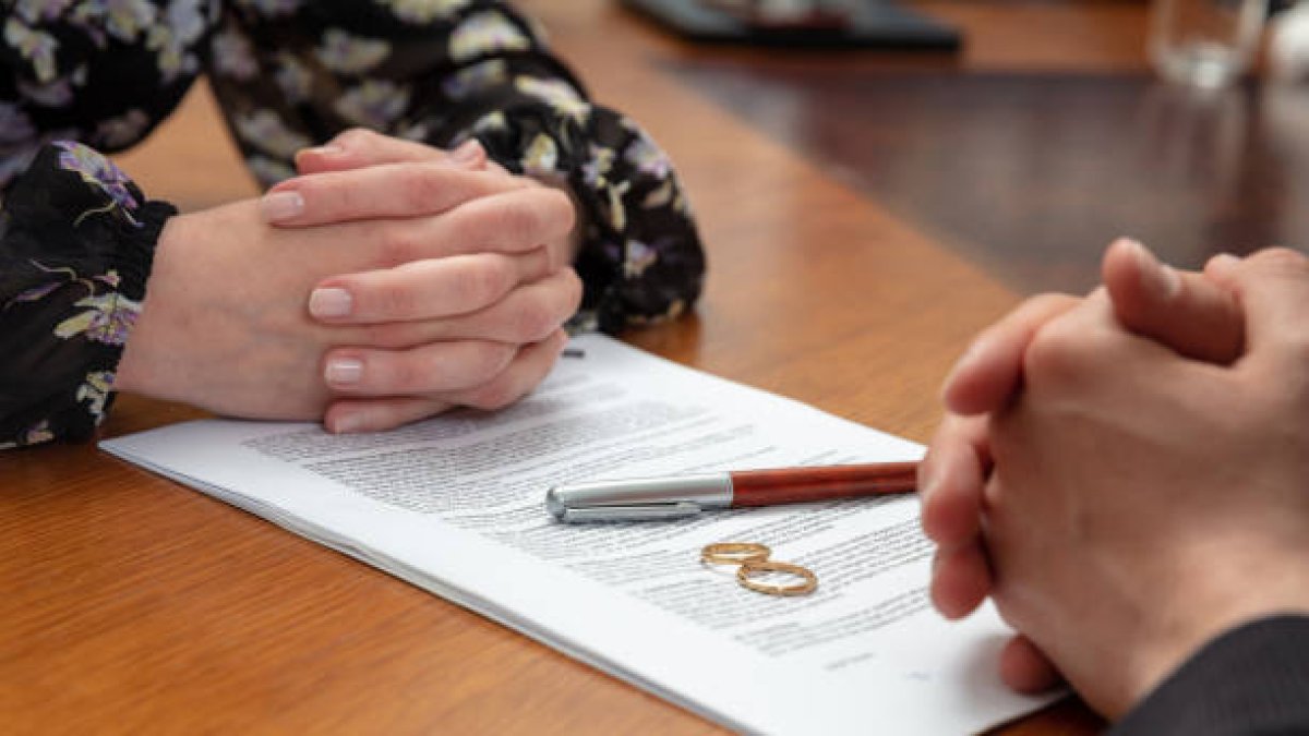 Signing a divorce, marriage dissolution documents and agreement. Wife and husband hands, wedding rings and legal papers for signature on a wooden table, lawyer offic
