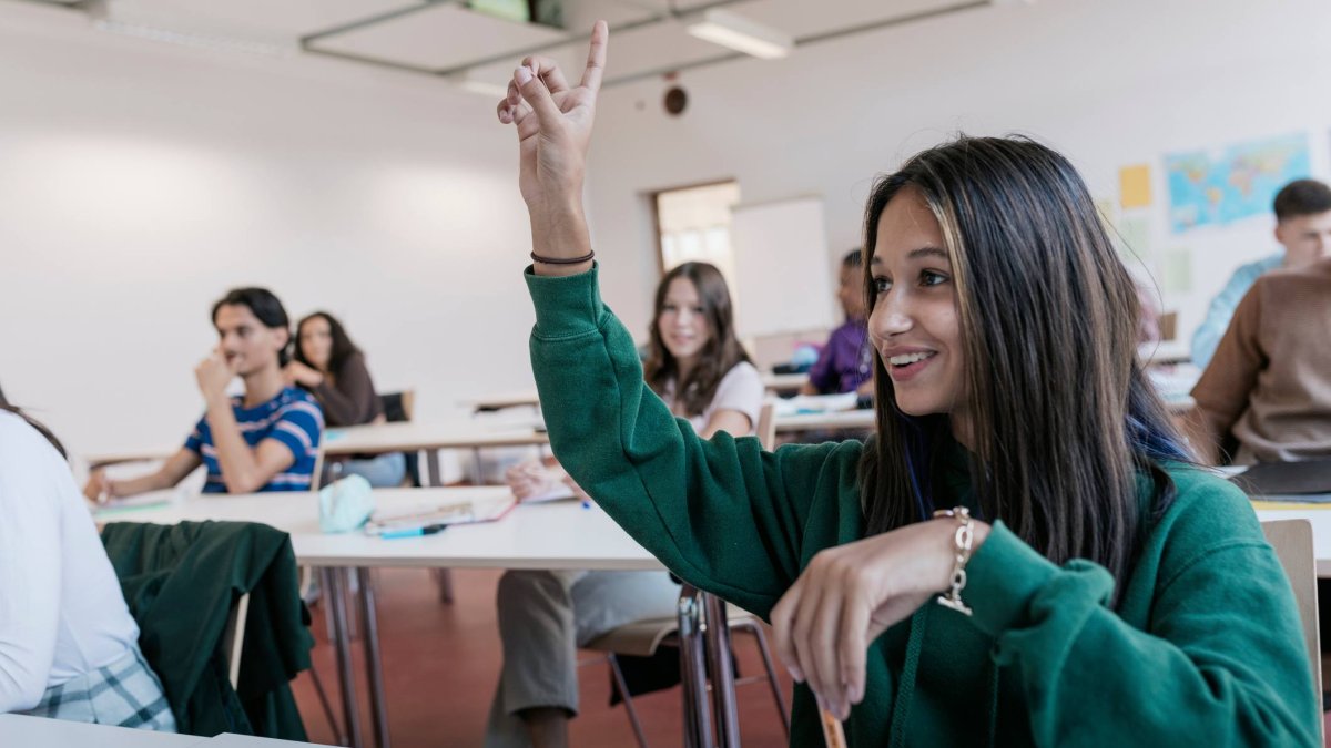 Una alumna interviene en el aula durante una clase, reflejando el contexto del estudio sobre cómo la dinámica entre compañeros influye en el rendimiento académico.