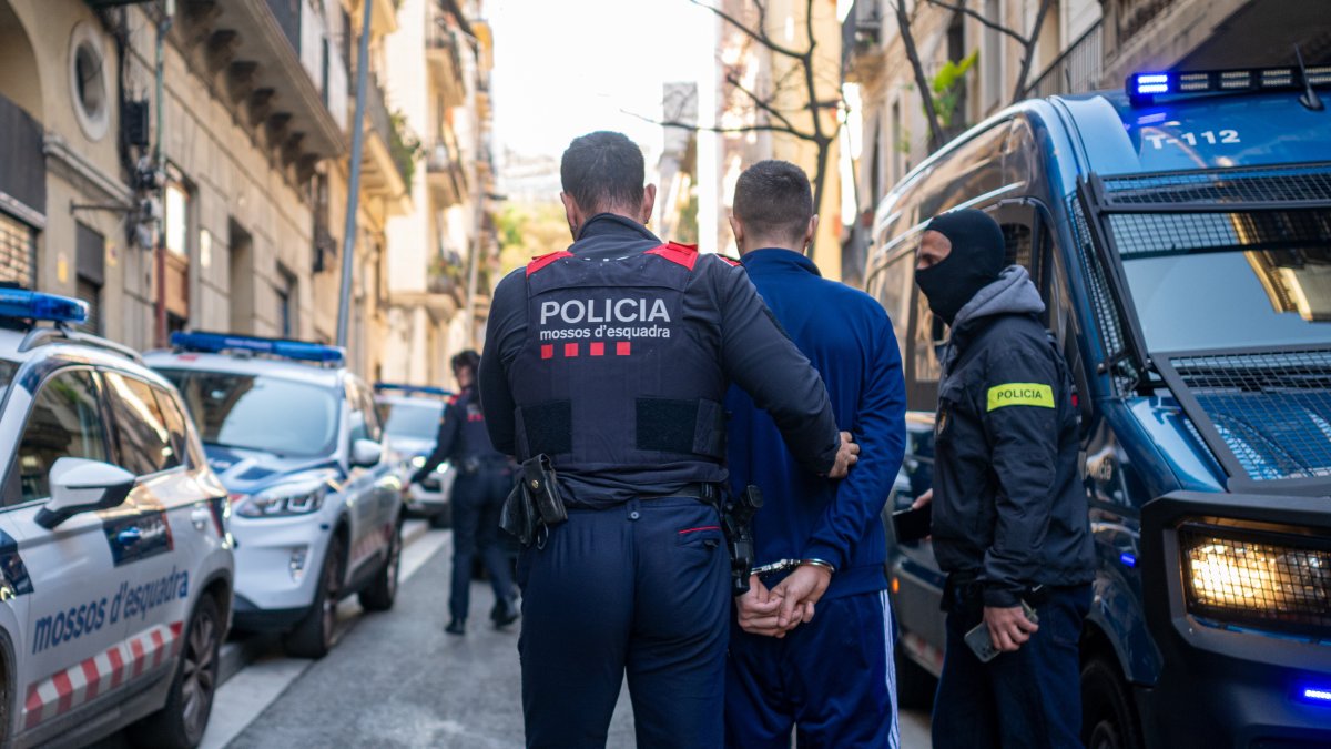 Un agente de los Mossos d'Esquadra se lleva a un detenido durante un operativo policial