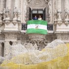 El presidente de la Junta de Andalucía, Juanma Moreno, despliega la bandera andaluza en el balcón principal de San Telmo, junto a la periodista Isabel Jiménez.