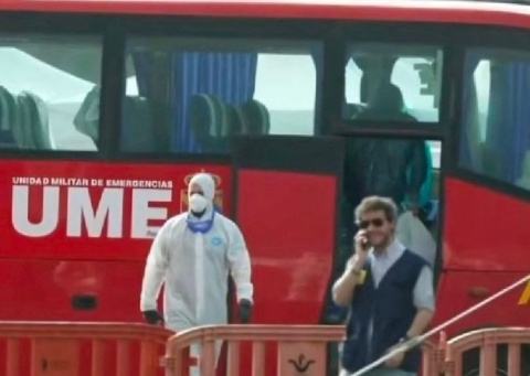 Un hombre charla sin protección junto a otro con EPI y el autobús de pasajeros del crucero con hantavirus abierto
